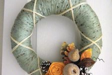 a chic yarn wreath with green yarn, fabric flowers and leaves and glitter fruit and snowy pinecones looks unusual