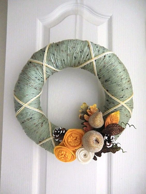 a chic yarn wreath with green yarn, fabric flowers and leaves and glitter fruit and snowy pinecones looks unusual