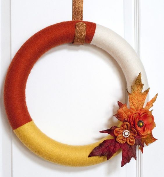a color block fall wreath covered with rust, yellow and white yarn, with faux blooms and leaves