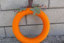 a colorful fall wreath covered with orange yarn, with fabric leaves and berries imitates a pumpkin