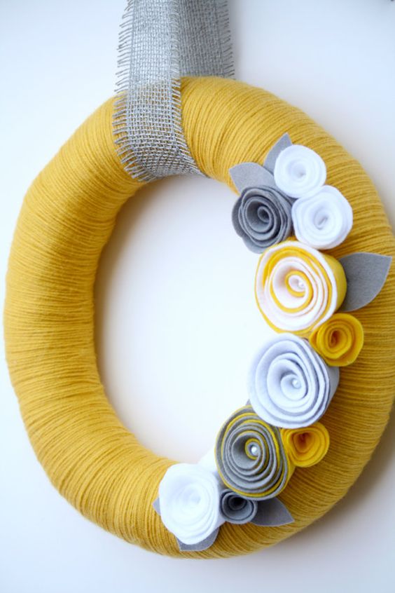 a colorful fall wreath covered with yellow yarn, fabric flowers and a burlap ribbon for a bold look