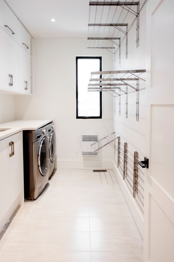 A contemporary white laundry with sleek cabinets and metal handles, a black washing machine and a dryer, metal wall mounted shelves