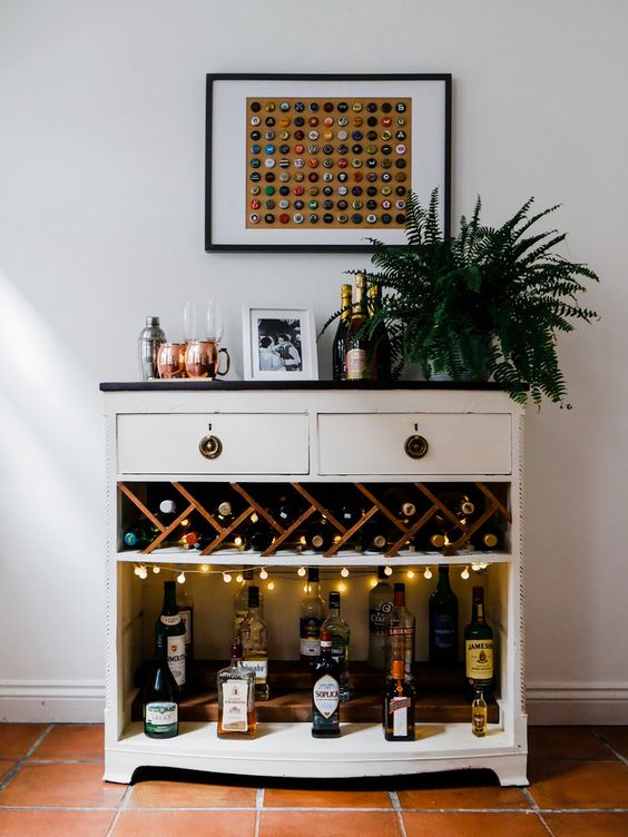 a cool bar unit with open space with lights, drawers and a potted plant plus a catchy artwork of lids