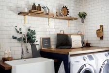 a cool modern laundry with black cabinets and stained countertops, an open shelf, a washing machine and a dryer, potted greenery