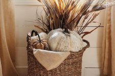 a fall basket styled with faux pumpkins, wheat, cane and burlap is a cool rustic arrangement