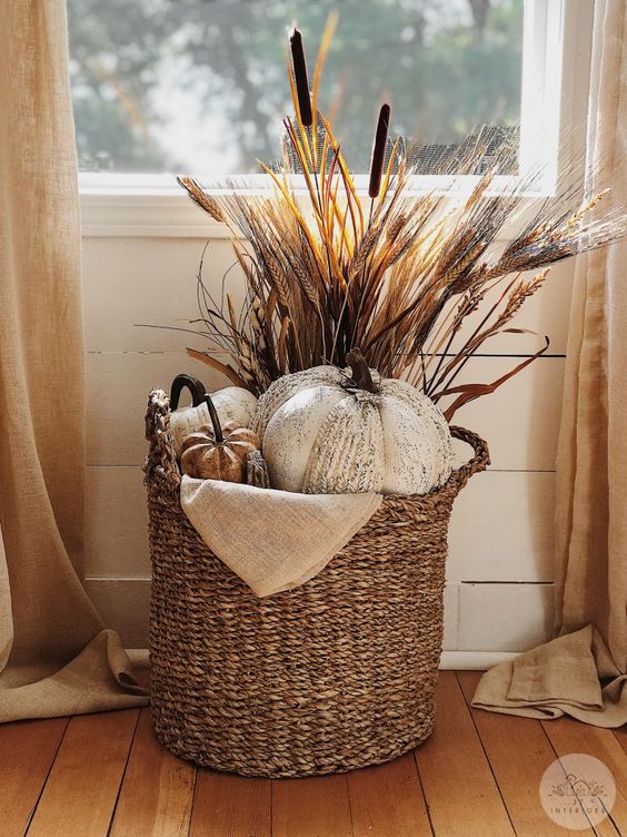 a fall basket styled with faux pumpkins, wheat, cane and burlap is a cool rustic arrangement