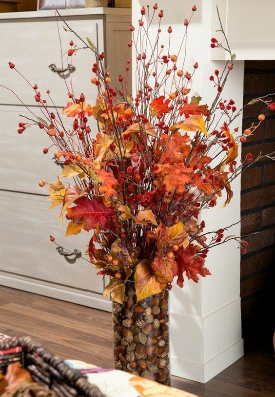 a fall centerpiece of a glass vase filled with nuts and acorns, with berry twigs and branches and fall leaves is very bright