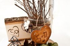 a fall centerpiece of a wood slice, moss, greenery, a wooden heart, a wooden piece and some branches and twigs in a glass vase