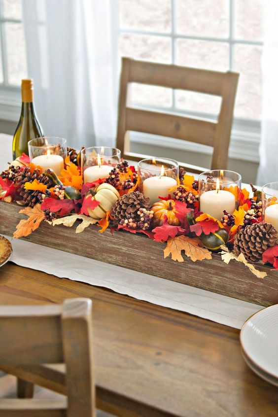 a fall centerpiece of a wooden box with pinecones, berries, fall leaves and candles in glass candle holders