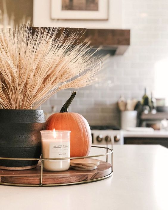 a fall centerpiece of a wooden tray, a candle in a jar, a pumpkin and wheat in a planter is a cool idea