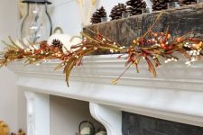 a fall mantel with berry branches, white pumpkins and wheat and some pinecones on the rough wood mantel