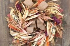 a fantastic rustic wreath of corn husks, corn cobs in bright colors, faux berries, wheat and a burlap bow on top