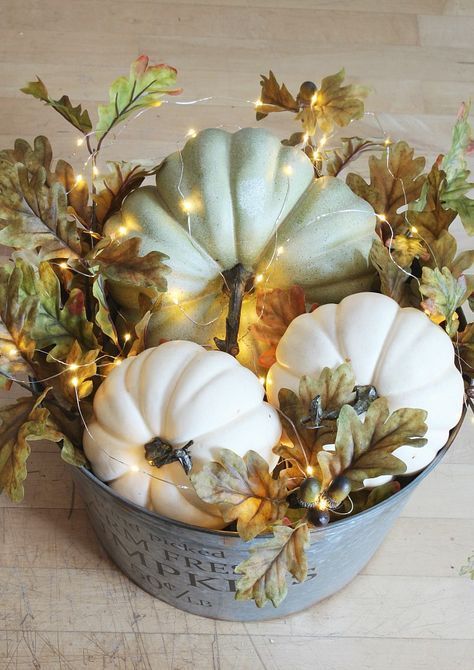 a farmhouse fall centerpiece of a bucket with fall leaves, acorns, faux pumpkins and lights is very cozy