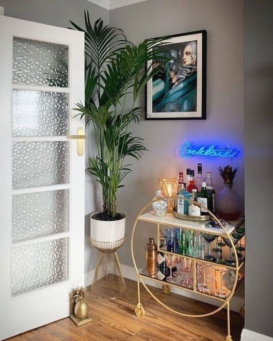 a glam home bar nook with a gold round bar with open storage spaces and a blue neon light over it
