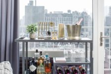 a grey bar cart with gold and brass touches, open storage compartments and a potted plant
