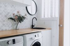 a lovely Scandinavian nursery with marble scallop tiles, a butcherblock countertop, a washing machine and a dryer, a cabinet and a round mirror