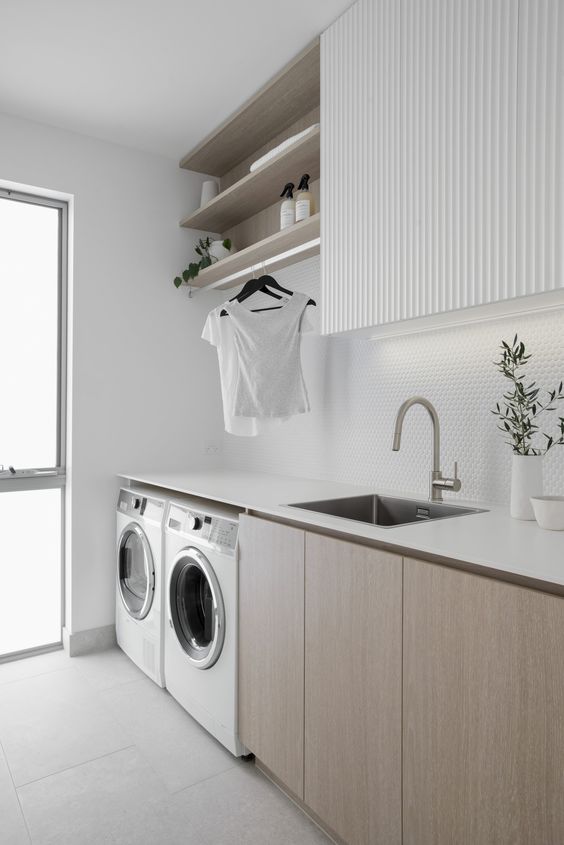 A minimalist neutral laundry with stained and white cabinets, a white penny tile backsplash and white appliances, built in lights