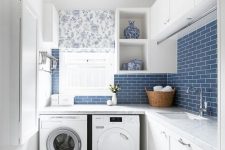 a modern farmhouse laundry with shaker style cabinets, stone countertops, a washing machine and a dryer, blue subway tiles and a floral curtain