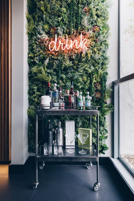 a modern home bar space with a green wall, a neon light and a metal cart with various drinks is very bold