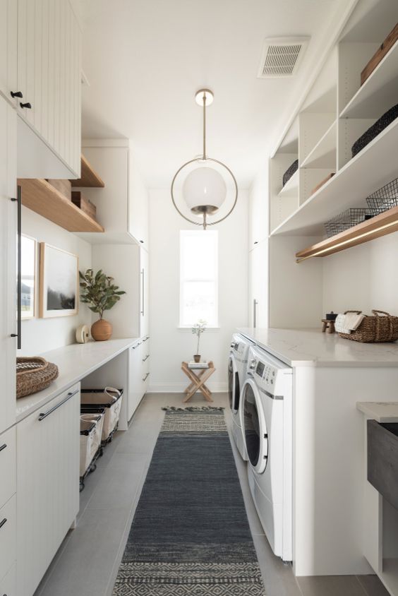 a modern neutral laundry with planked cabinets, open shelves, a console table and baskets, stained shelves and a washing machine and a dryer (designed by Urbanology Designs)