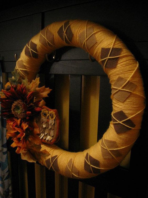 a moody fall wreath covered with orange yarn, brown fabric rhombs and faux blooms and leaves plus a play owl
