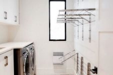 a neutral laundry with sleke cabinets, a white countertop, lots of holders for clothes and clothes hangers and a small window