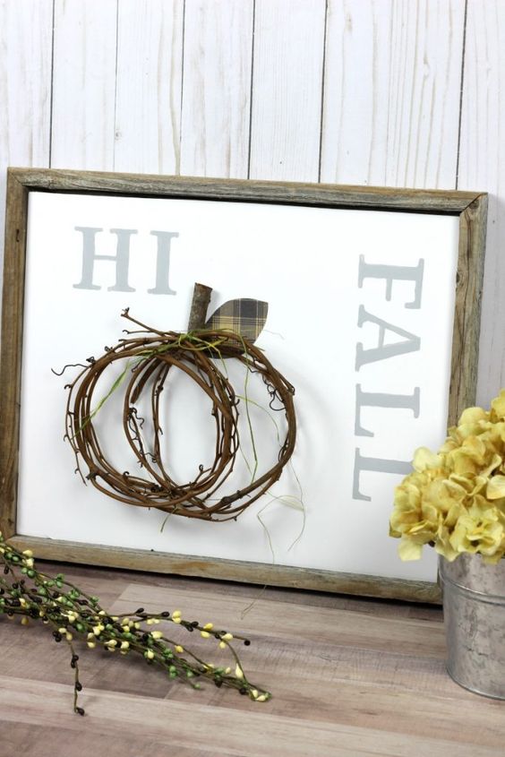 A non typical fall sign in a reclaimed wooden frame, a twig pumpkin attached and yellow blooms next to it