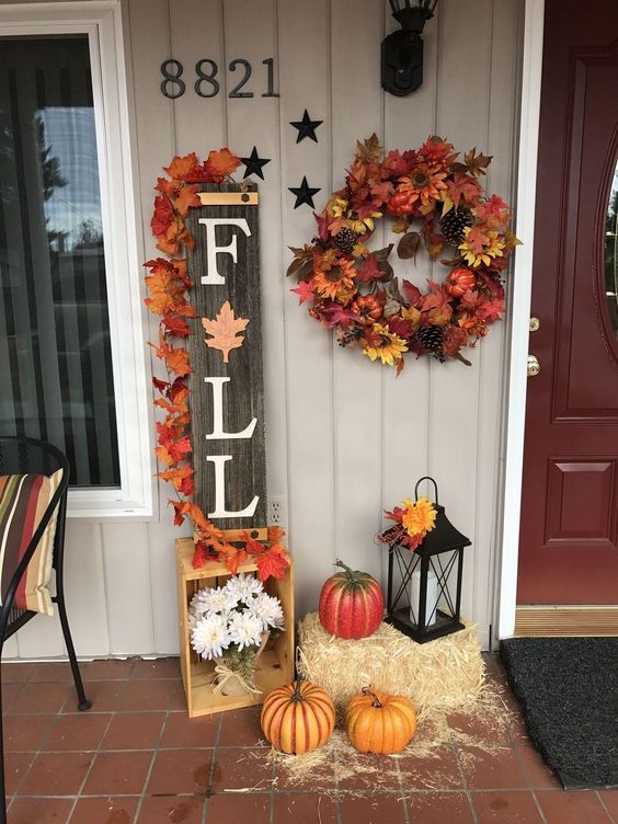 a reclaimed wood Fall sign topped with bright fake leaves, faux pumpkins, a wreath, hay and a lantern
