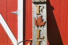 a reclaimed wood Fall sign with yellow letters and a red leaf, pumpkins and a basket with leaves