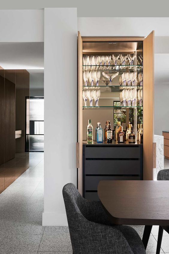 A refined built in home bar with a mirror backsplash, glass shelves, sleek drawers and built in lights