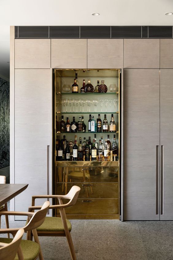 A refined built in home bar with glass shelves and sleek gold drawers for storage is super chic