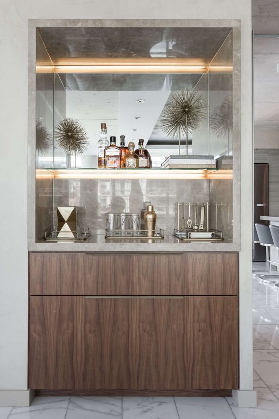A refined built in home bar with neutral marble, lit up shelves and sleek drawers is very chic and stylish