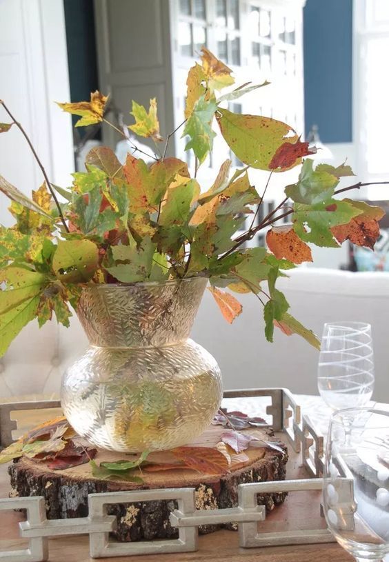 A simple and all natural fall centerpiece of a clear vase with fall leaves put on a wooden slice