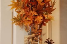 a simple fall centerpiece of a glass vase with wine corks and fall leaves on branches can be DIYed fast