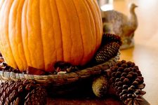 a simple fall centerpiece of a wood board, pinecones and a pumpkin in a woven tray is easy to make