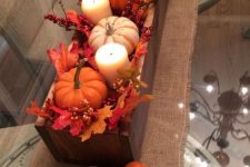 a simple fall centerpiece of a wooden box, with faux leaves, berries, pumpkins and pillar candles