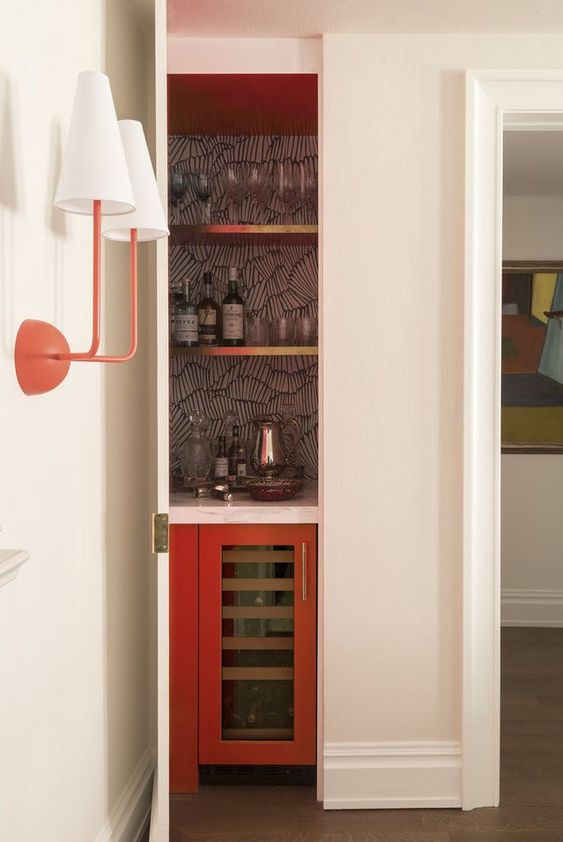 a small hidden bar with a wallpaper backsplash, open gold shelves and a fridge is chic and cool