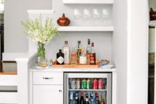 a small home bar with a fridge, drawers, open shelves and some blooms in a vase is a cool idea