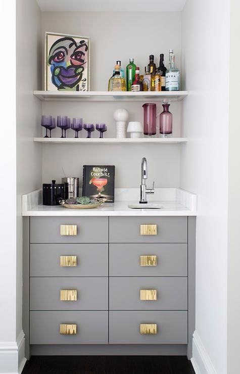 A small yet chic built in bar with a sink, open shelves, drawers and a marble countertop plus colorful glass