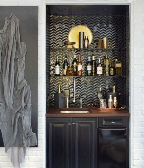 A small yet refined built in bar with a tile backsplash, a black cabinet with a sink and touches of gold
