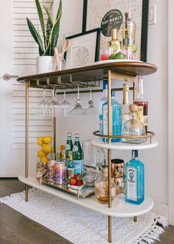 a stylish bar cart in brass, with open storage compartments, some artworks and a potted plant