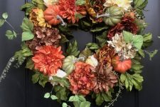 a stylish fall wreath of greenery, faux pumpkins and bright blooms is a cool decoration to rock