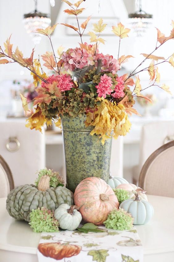 a stylish rustic fall decoration of a bucket with pink and green faux blooms, branches with leaves and heirloom pumpkins