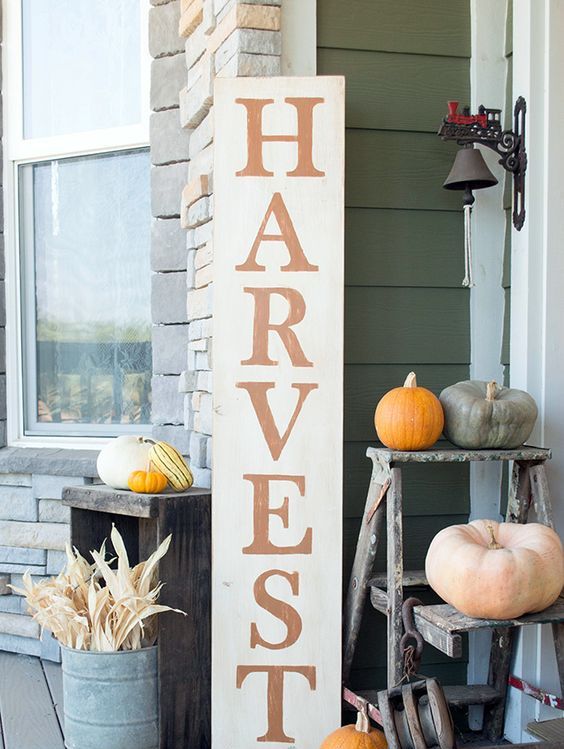 a tall Harvest sign, corn husks in a bucket and various colorful pumpkins around for a fall feel