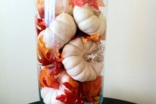 a tall glass vase with white pumpkins and bright fall leaves is a very easy arrangement for a bold look