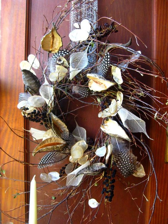 a twig fall wreath with dried leaves, blooms, feathers and berries looks boho-like and woodland-inspired