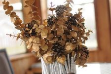 a vase covered with silver painted sticks and twigs, dried eucalyptus and pinecones is a chic fall centerpiece