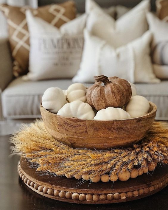 a wheat wreath surrounding a wooden bowl with white pumpkins and a wooden one for the fall