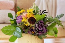 a white pumpkin with foliage, faux yellow and purple blooms and some dried touches is a chic fall centerpiece