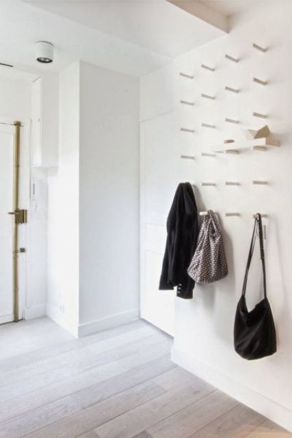 a white wall with lot sof hooks to hang clothes and bags or even place shelves and store shoes on them